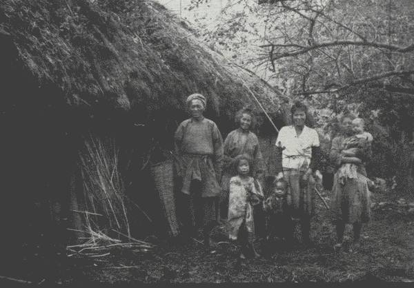 HAPPY FAMILY IN BACKWOODS  The Author spent two nights in this crudely-thatched home in the hills. Though poor, the people were extremely hospitable—and invariably happy.