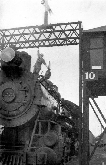 A man in a suit hangs between a trestle and a train.