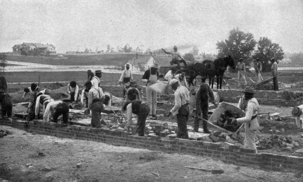 STARTING A NEW BUILDING.  Student masons laying the foundation in brick.