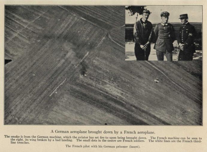 A German aeroplane brought down by a French aeroplane. The smoke is from the German machine, which the aviator has set fire to upon being brought down.  The French machine can be seen to the right, its wing broken by a bad landing.  The small dots in the center are French soldiers.  The white lines are the French third-line trenches. The French pilot with his German prisoner (insert).
