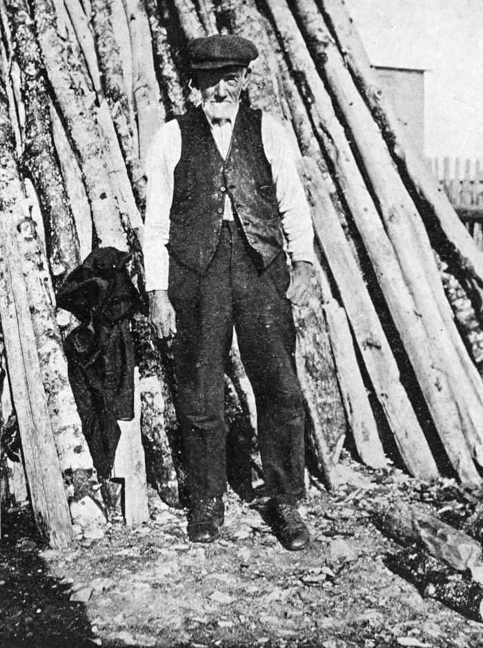 Photo full of man standing in front of very tall woodpile