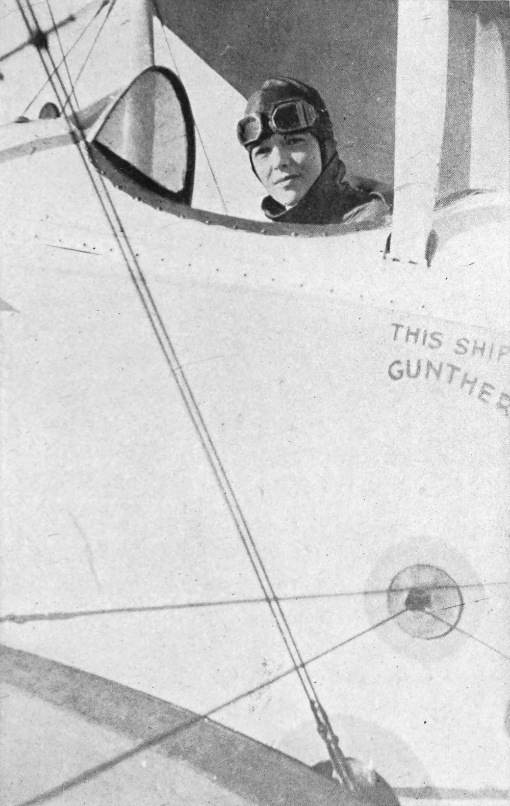 Photo medium shot of Earhart wearing flight gear looking out from a biplane