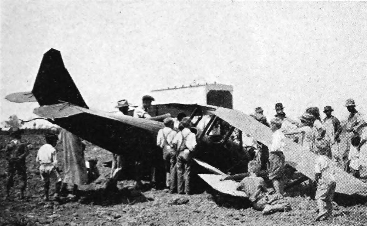 Photo wide shot of crowds surrounding a crashed biplane