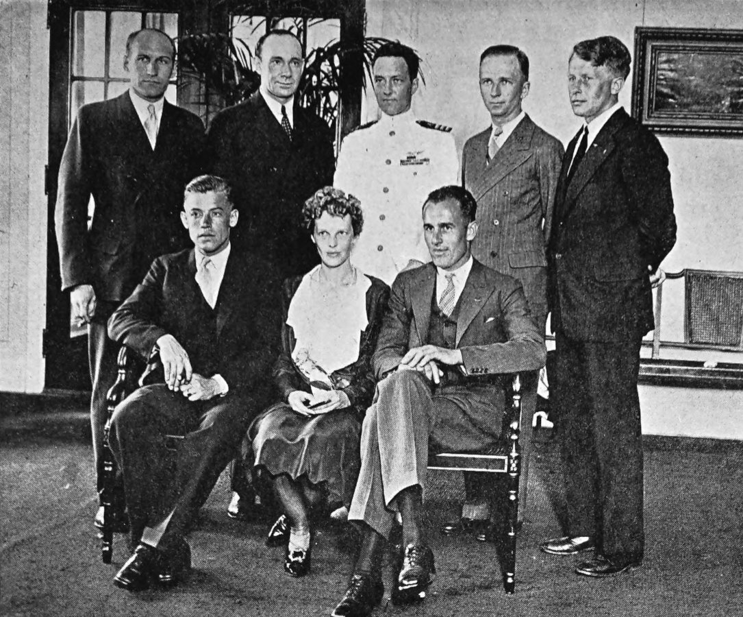 Photo wide indoor shot of 8 individuals;                 Stultz, Earhart, Gordon are seated; 5 are standing in                 back