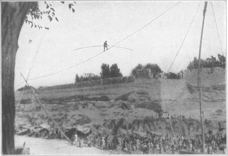 A tightrope walking high above a large group of people and tents.