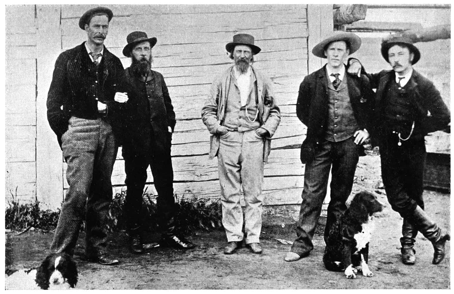 5 men standing with dogs sitting nearby