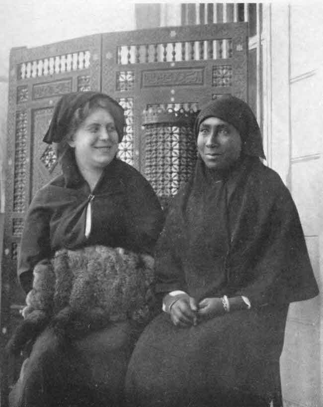  The author is shown seated with Miss Chocolate, both in long covering attire with their hair covered.