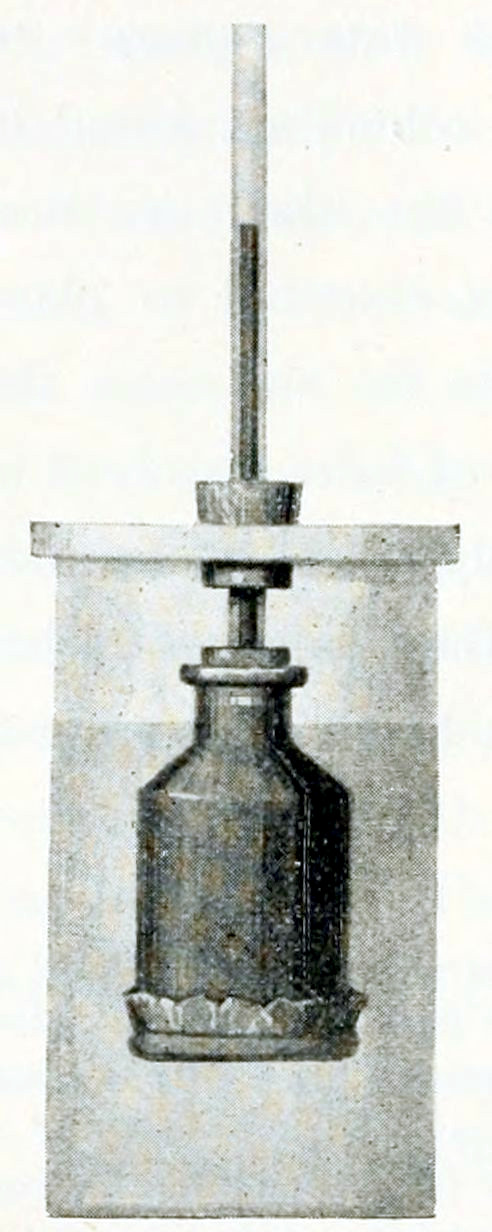 A cylinder standing vertically, covered with a lid. Through the lid a cork protrudes. Through the cork extends a thin tube. At the bottom side this tube ends in a small flask that is hanging in the cylinder. The bottom of the flask is made of foil, fastened by a thin ring. The cylinder is filled with a liquid up to a level reaching the neck of the flask. The flask contains a darker liquid the extends upward through the tube, up to a level above the lid. The upper border of that liquid is shown.