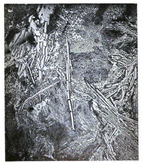 Micrograph showing a complex, dense metal microstructure with needle-like and rod-like crystalline formations at various angles, along with wavy grain patterns.