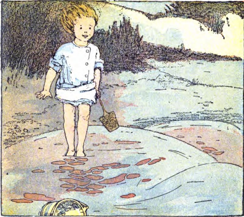 A young child with blond hair stands on wet sand near the water. The child holds a small wooden shovel. The child wears a light blue short-sleeved smock over white shorts or undergarments. In front are small shallow puddles with reddish water. Sand dunes and green shrubs fill the background. At the bottom, part of a bucket lies on its side.