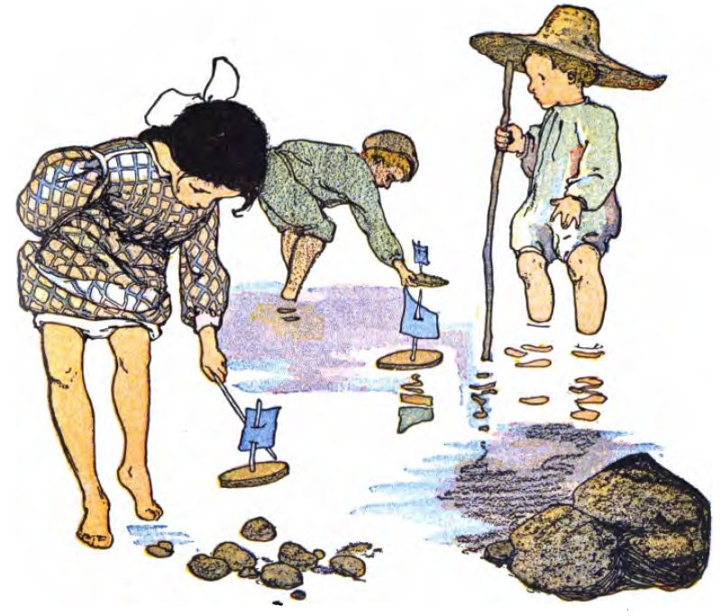 The image shows three young children playing barefoot in a shallow pool of water against a plain white background. On the left, a girl with a white bow in her dark hair wears a patterned tunic. She leans forward and uses a stick to guide a small boat with a blue sail. In the center, a boy in a green tunic and cap bends over the water to adjust a wooden boat with a light-blue sail. On the right, another boy stands upright in a light-colored tunic and an oversized straw hat. He holds a long walking stick and watches the others. The children sail simple homemade toy boats made from flat pieces of wood, twig masts, and small paper or cloth sails. In the bottom right corner, a cluster of smooth grey river rocks sits, with a few smaller pebbles scattered near the girl's feet.