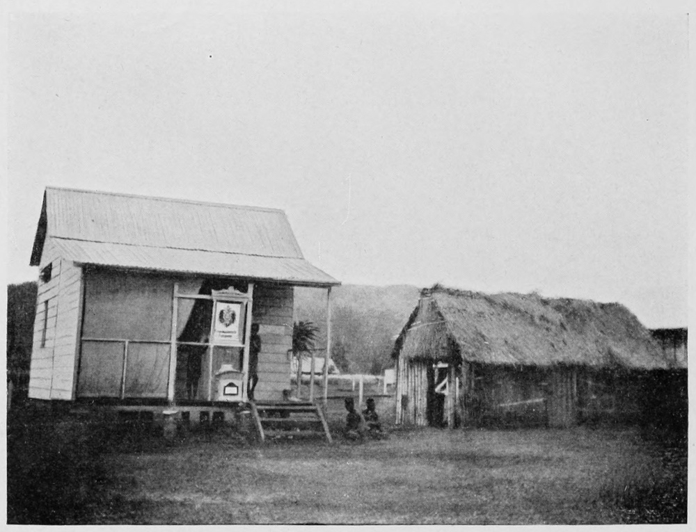 Rustic building with a door and one window, next to a smaller thatched roof building