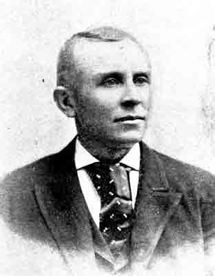 Deep-set eyes; matching suit jacket and vest, patterned tie with wide double windsor knot.