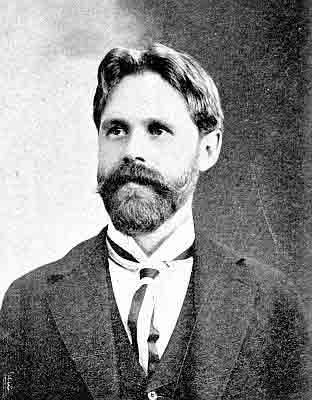 Neatly trimmed beard with droopy walrus moustache; wide stripes in half-Windsor tie.