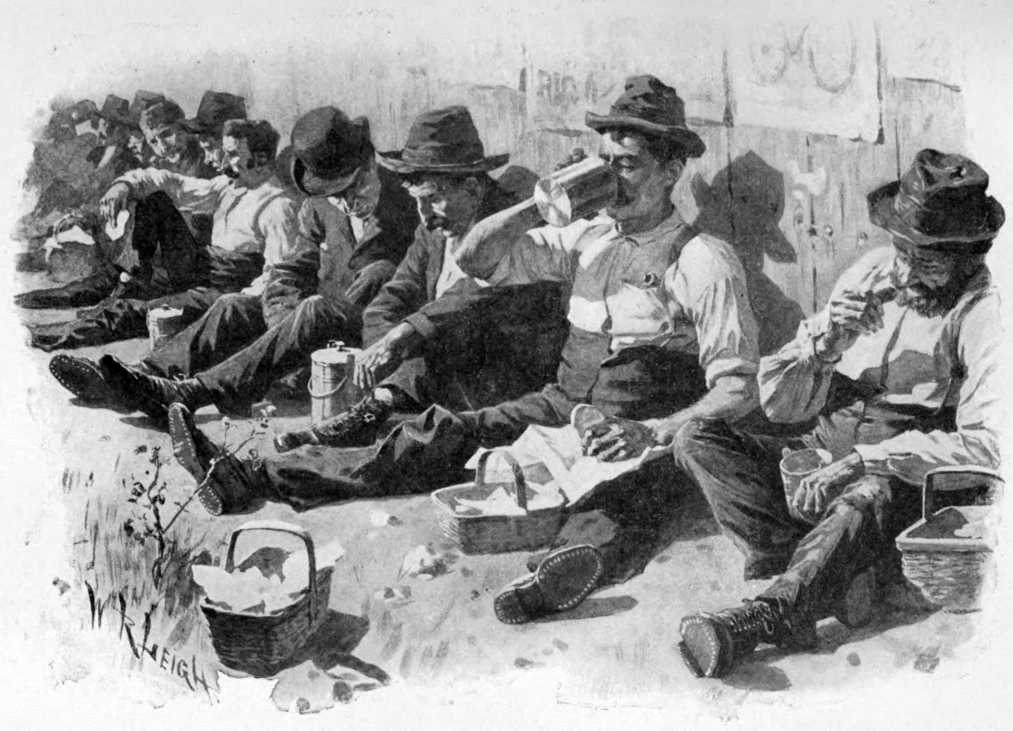 A long line of men sitting with their backs against a
wall having lunch.