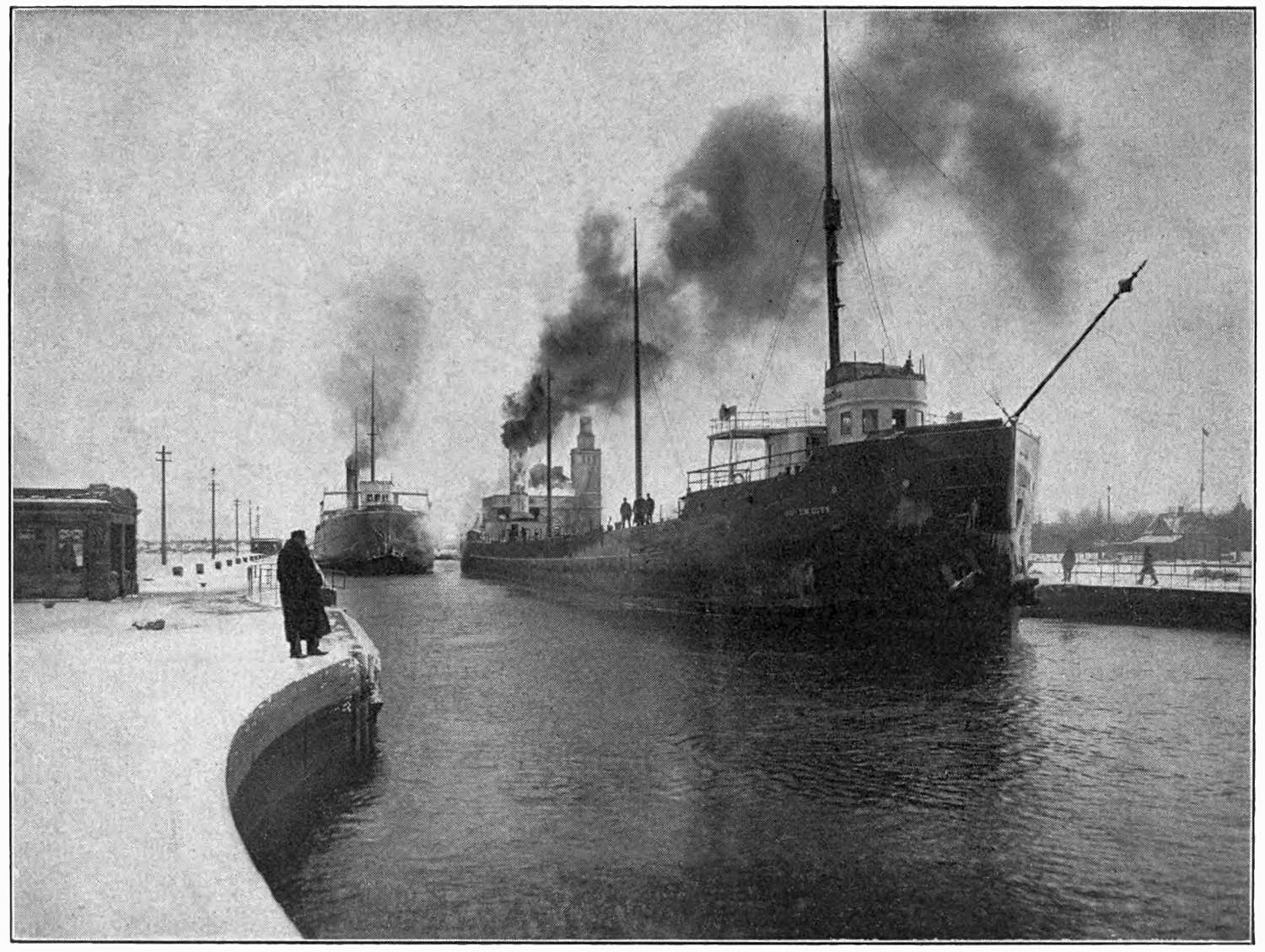 Photograph of ships in a canal taken from shore.
