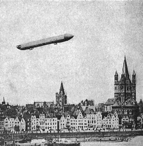 A photograph
of a Zeppelin airship flying over a German city skyline with Gothic
church spires and gabled rooftops — likely Cologne — an early
20th-century image of rigid airship travel over the Rhine.