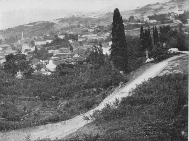 The view in this photo is
from a hill overlooking the town, with what appears to be an empty dirt road
nearer to the camera than the town and running through vegetation on the hillside,
including trees.