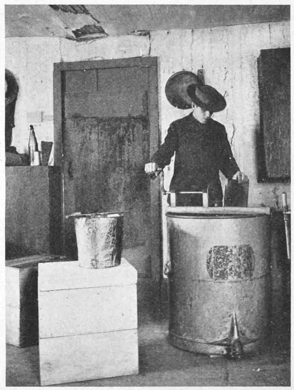 In the same room the person is putting the frame into the extractor. The extractor is a metal barrel about the size of a steel drum, with a handle at the top.